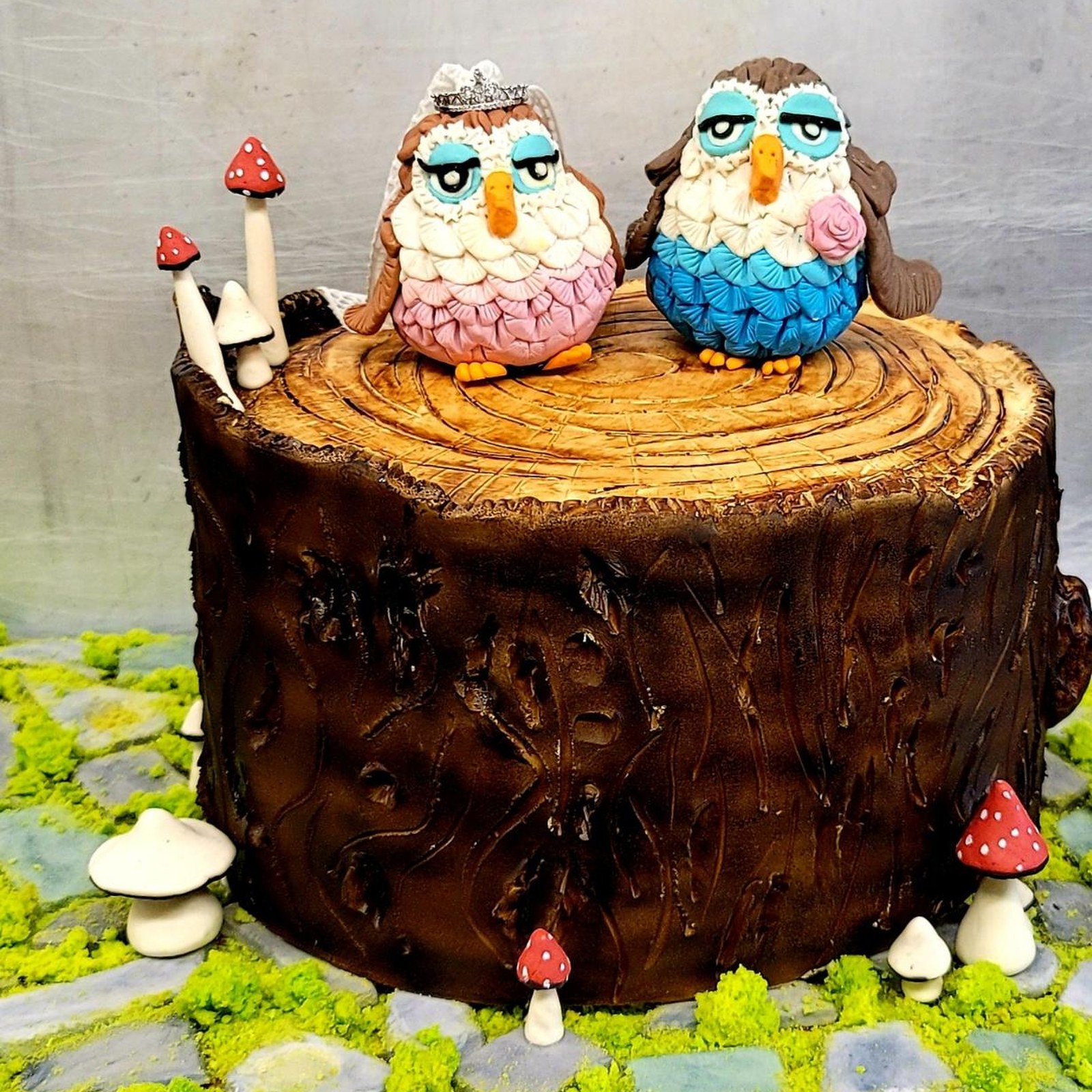 A tree-stump wedding cake topped with two fondant owls, one in a veil, surrounded by mushrooms and moss