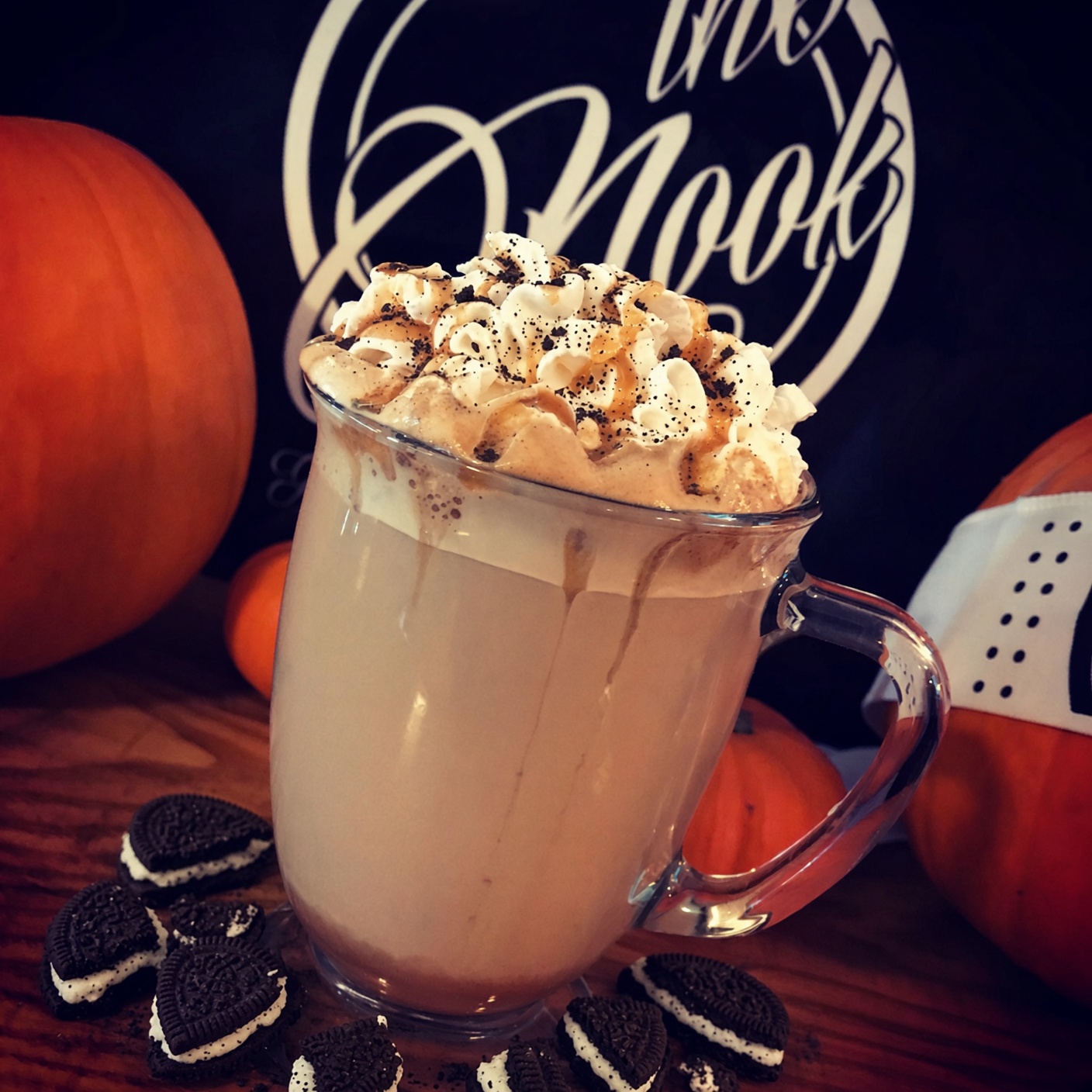 A glass mug of hot chocolate with whipped cream, Oreo dust, and crumbled Oreos