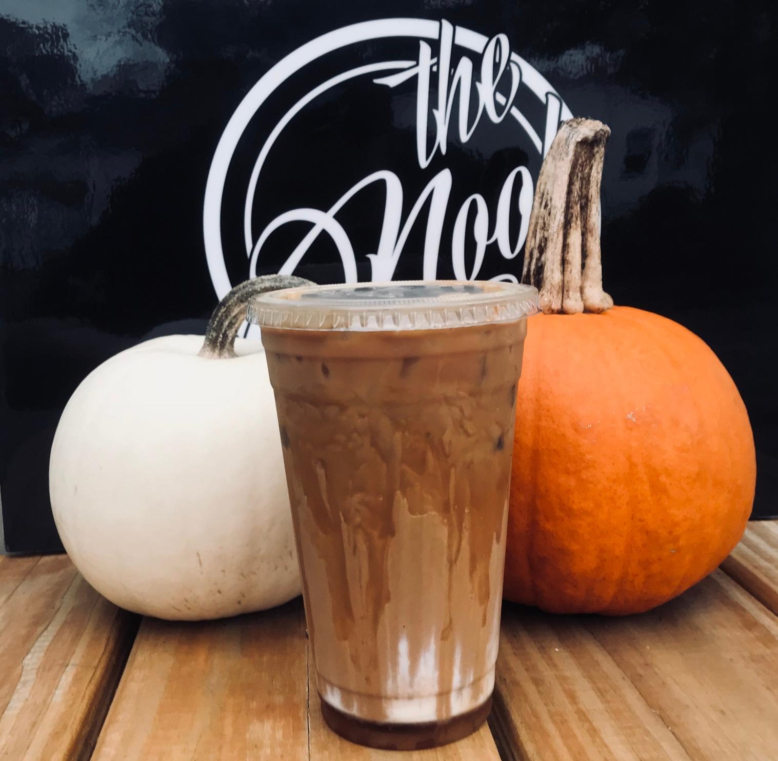 An iced Real Pumpkin Latte between a white pumpkin and an orange pumpkin